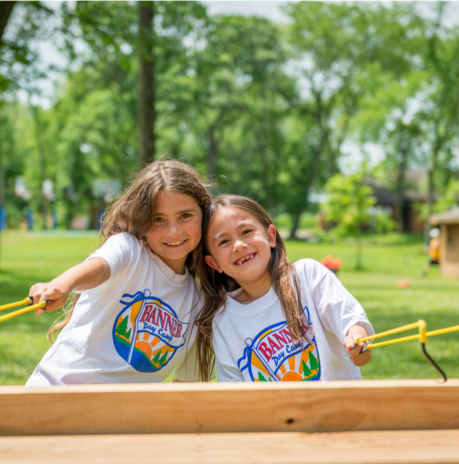 Two girl campers smiling together at the sling shot station